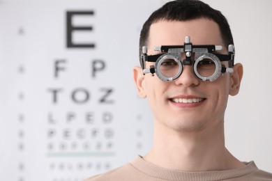 Young man with trial frame against vision test chart