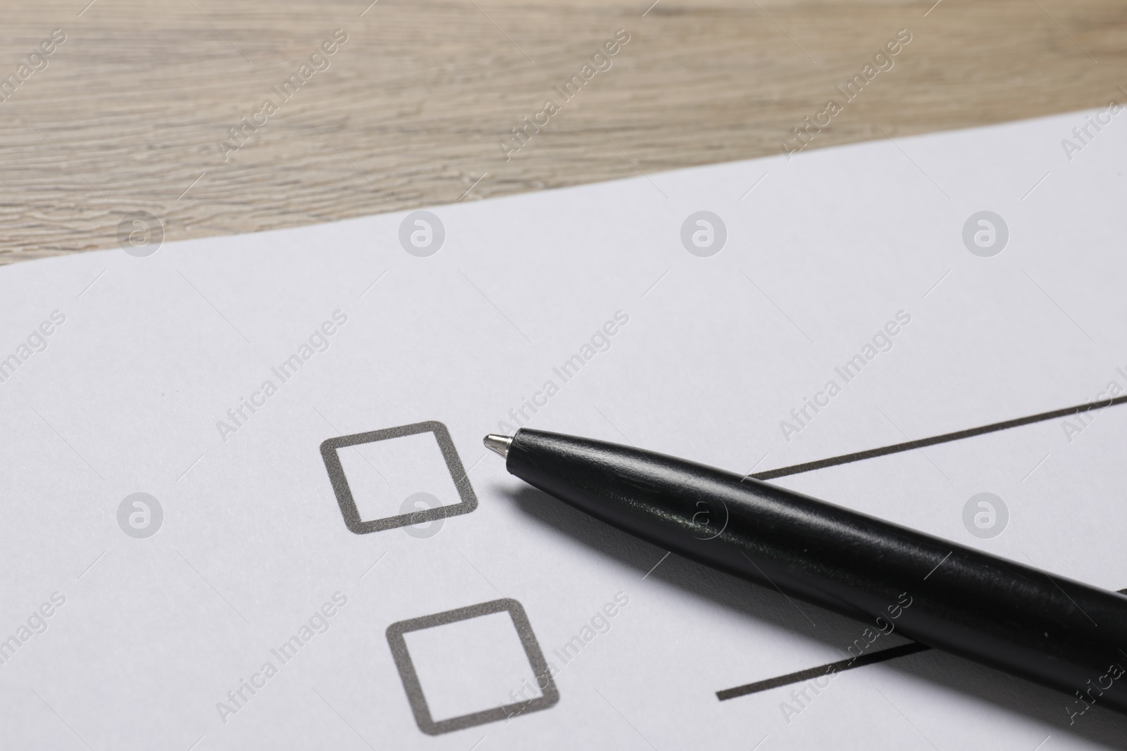 Photo of Paper sheet with checkboxes and pen on wooden table, closeup. Checklist