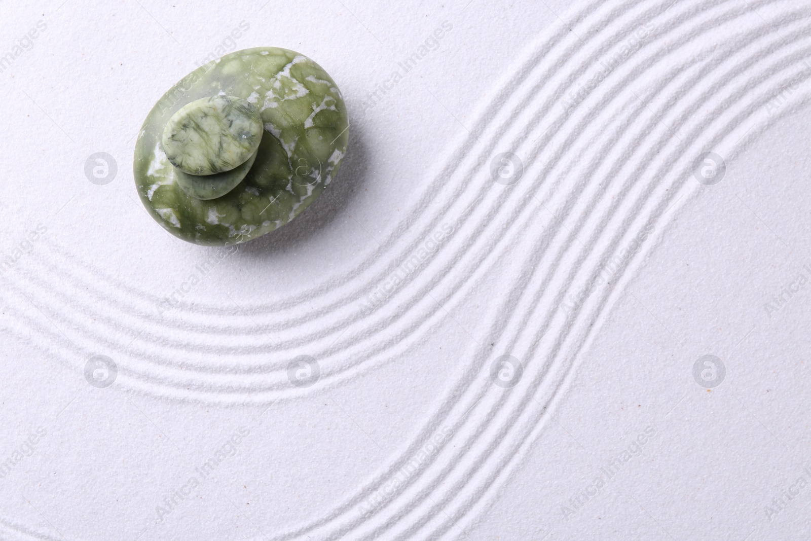 Photo of Zen garden stones on white sand with pattern, top view. Space for text