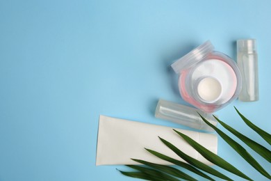 Photo of Cosmetic products and palm leaves on light blue background, flat lay. Space for text
