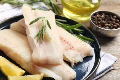 Photo of Pieces of raw cod fish, rosemary and lemon on wooden table, closeup