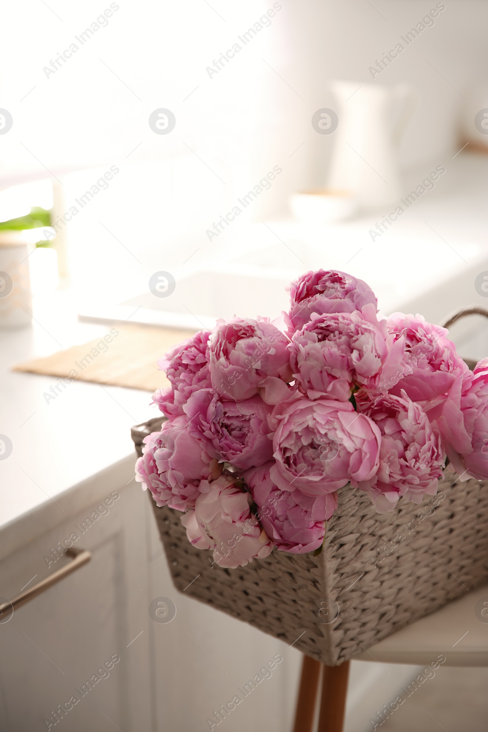 Photo of Basket with beautiful pink peonies in kitchen
