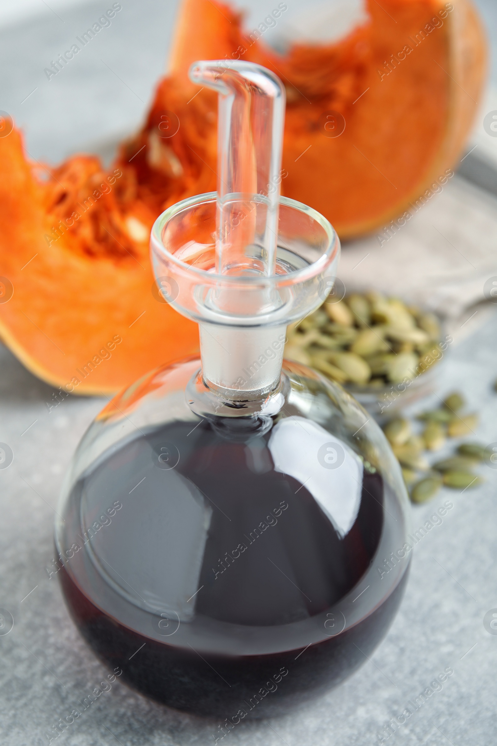 Photo of Laboratory glassware of oil with cut pumpkin and seeds on light grey table, closeup