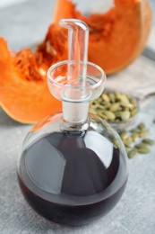 Photo of Laboratory glassware of oil with cut pumpkin and seeds on light grey table, closeup