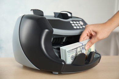 Photo of Woman taking money from counting machine at table indoors, closeup