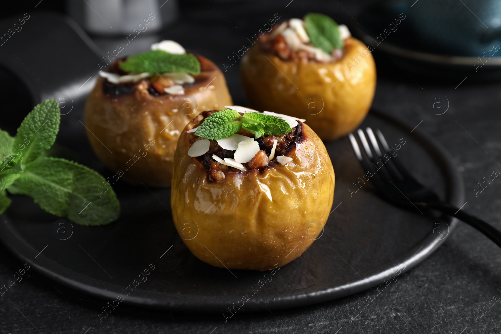 Photo of Delicious baked apples with nuts and mint served on black table