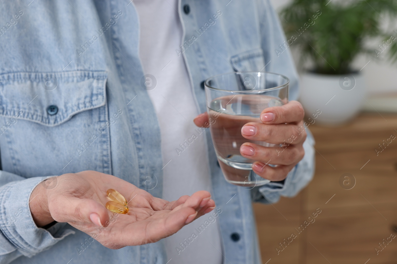 Photo of Woman with vitamin pills and glass of water indoors, closeup