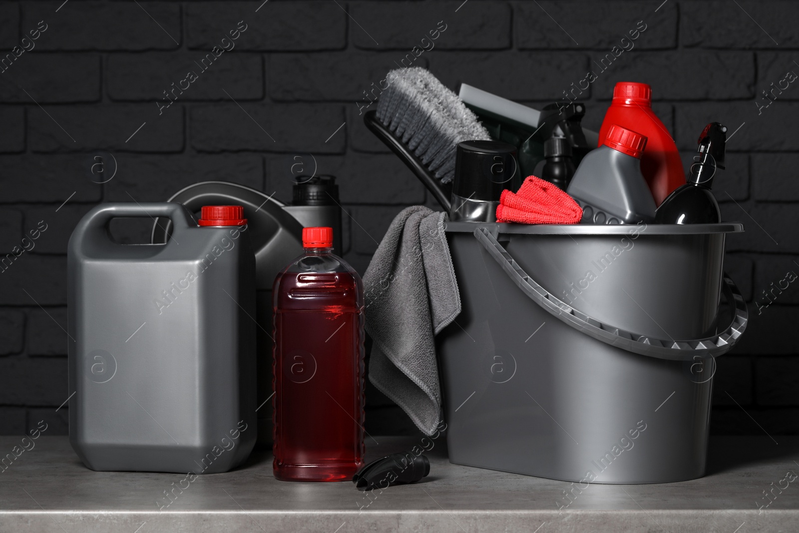 Photo of Different car cleaning products on grey table near black brick wall