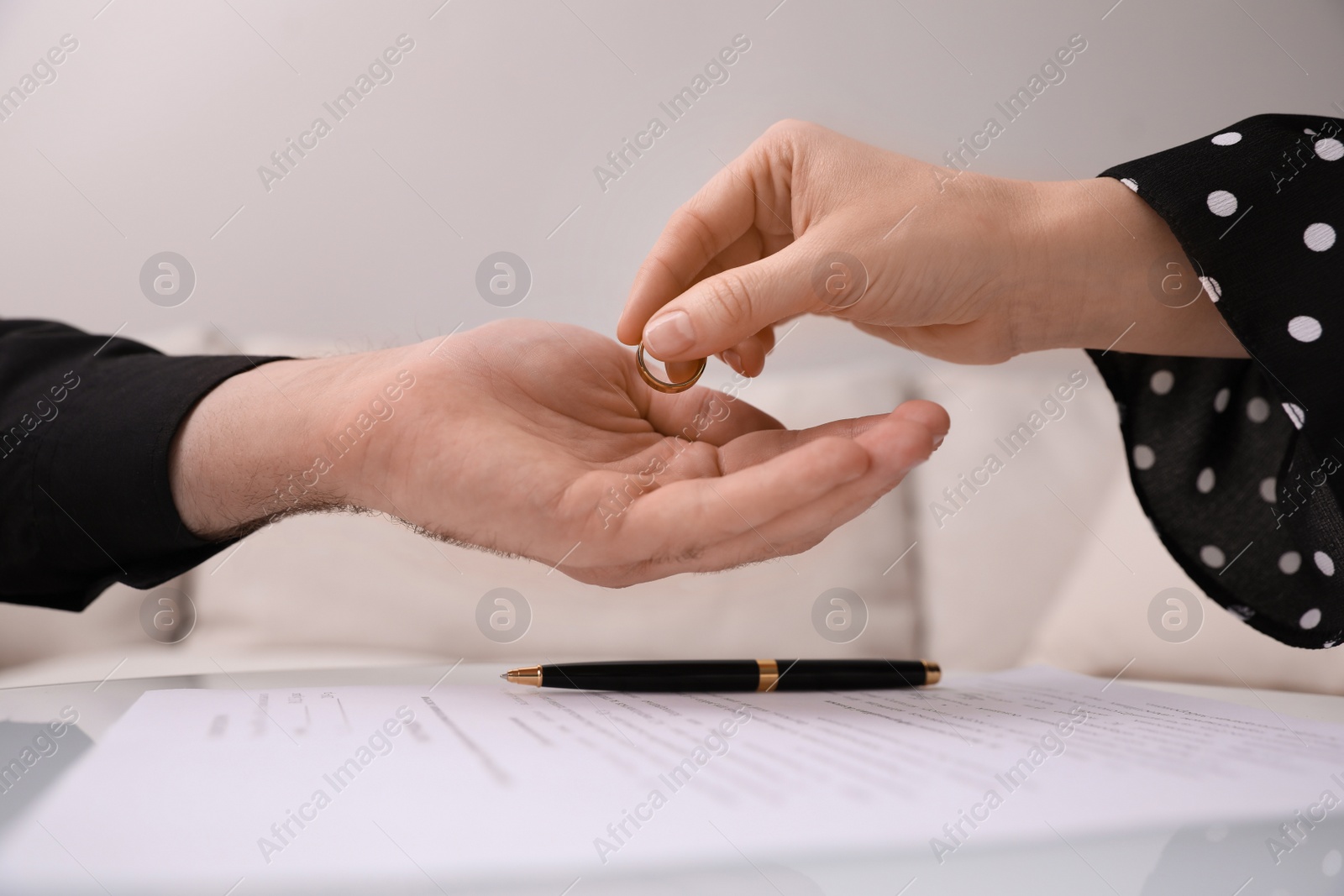 Photo of Woman giving wedding ring to her husband over divorce papers indoors, closeup