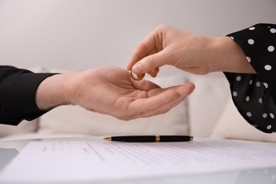 Woman giving wedding ring to her husband over divorce papers indoors, closeup