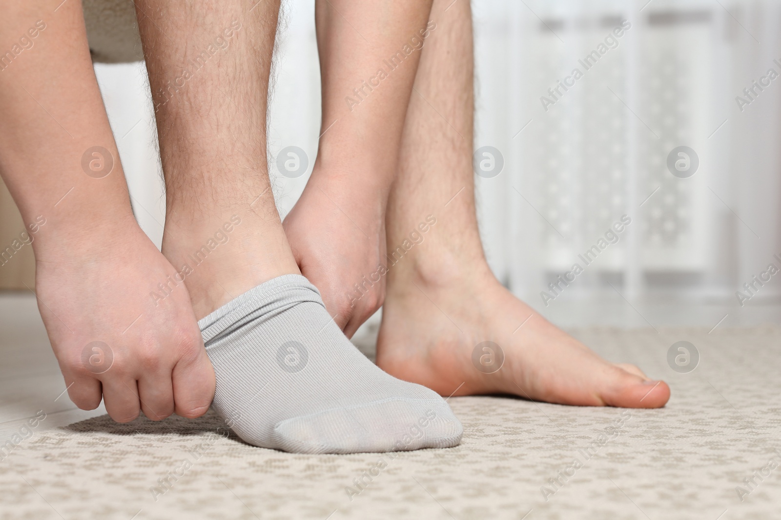 Photo of Man putting on light socks at home, closeup