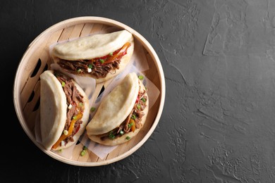 Delicious gua bao in bamboo steamer on black table, top view. Space for text
