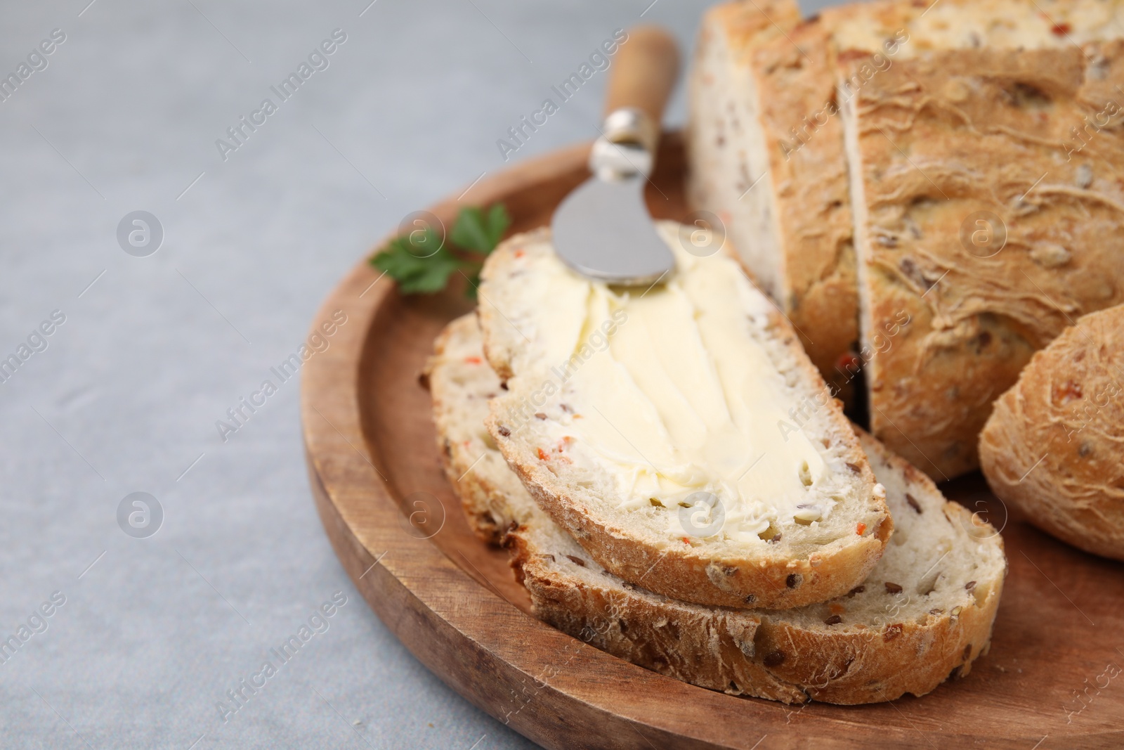 Photo of Tasty bread with butter and knife on grey table, closeup. Space for text