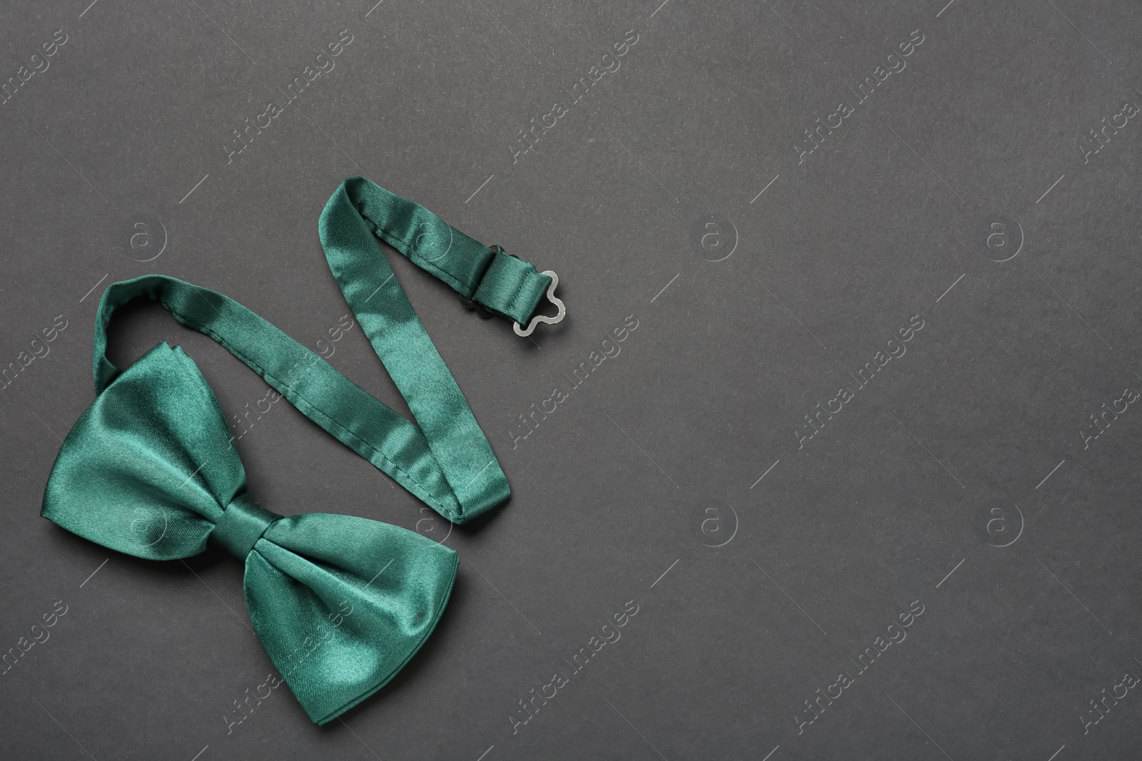 Photo of Stylish green satin bow tie on dark background, top view. Space for text