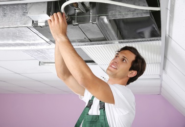 Photo of Young male technician repairing air conditioner indoors