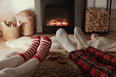 Photo of Couple in knitted socks near fireplace at home, closeup of legs