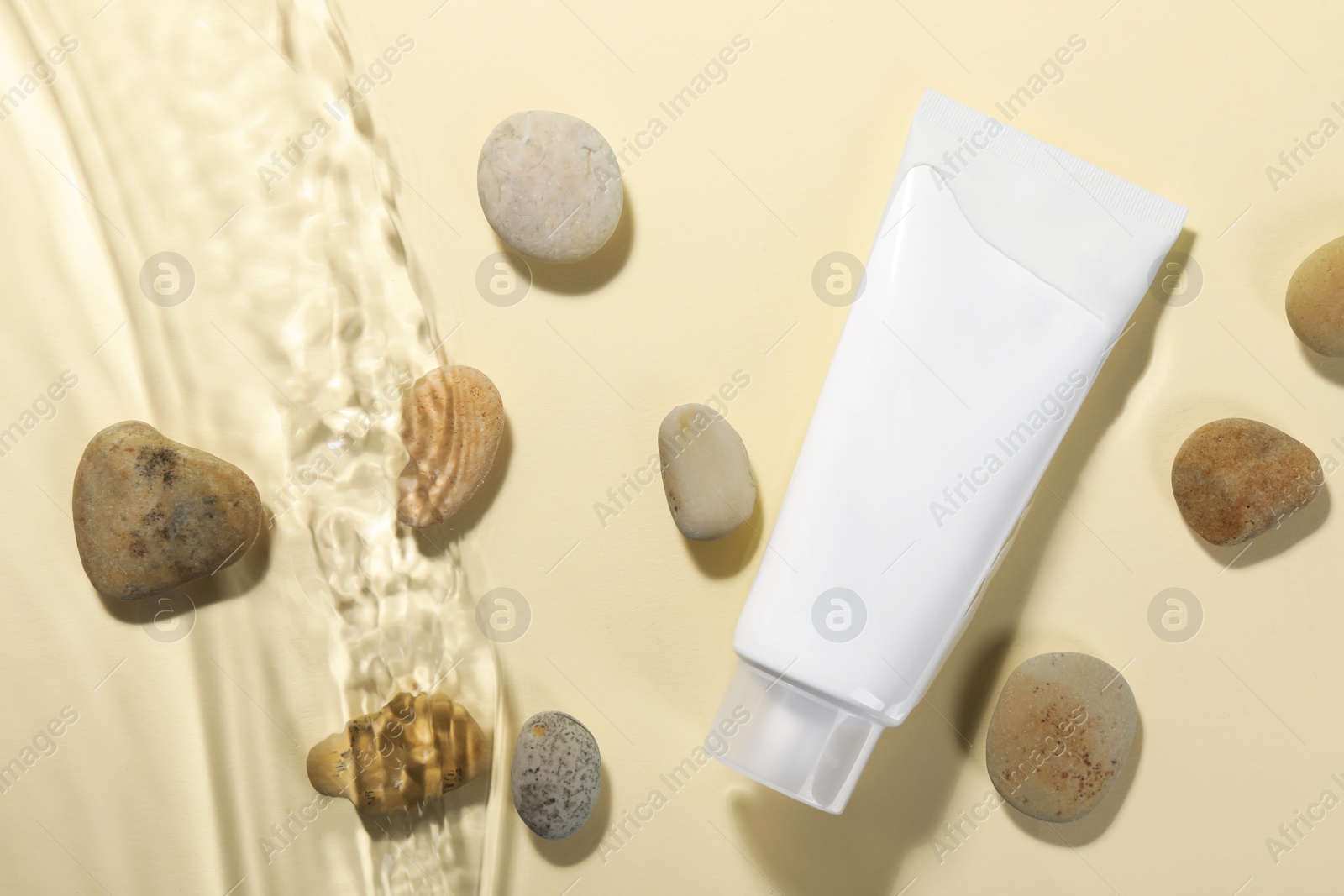 Photo of Tube of face cleansing product and stones in water against beige background, flat lay