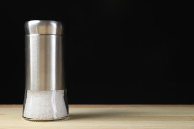 Photo of Salt shaker on light wooden table against black background. Space for text