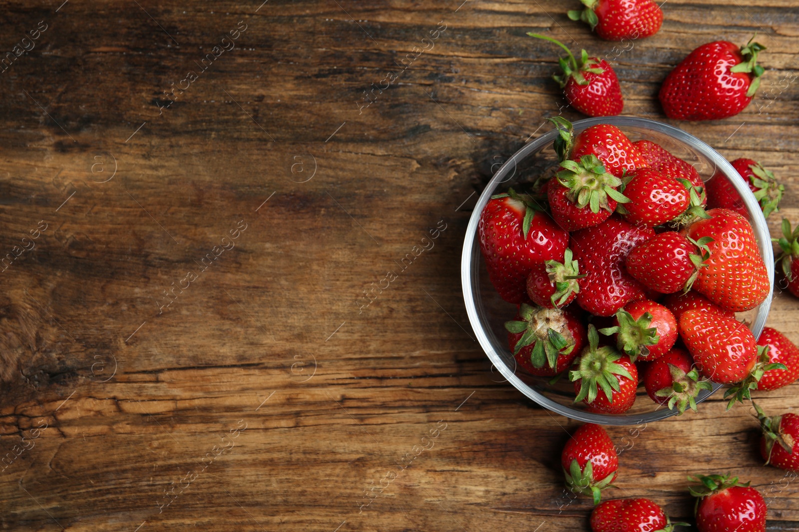 Photo of Delicious ripe strawberries in glass bowl on wooden table, flat lay. Space for text