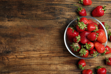 Delicious ripe strawberries in glass bowl on wooden table, flat lay. Space for text