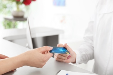 Photo of Woman giving credit card to receptionist at desk in beauty salon, closeup