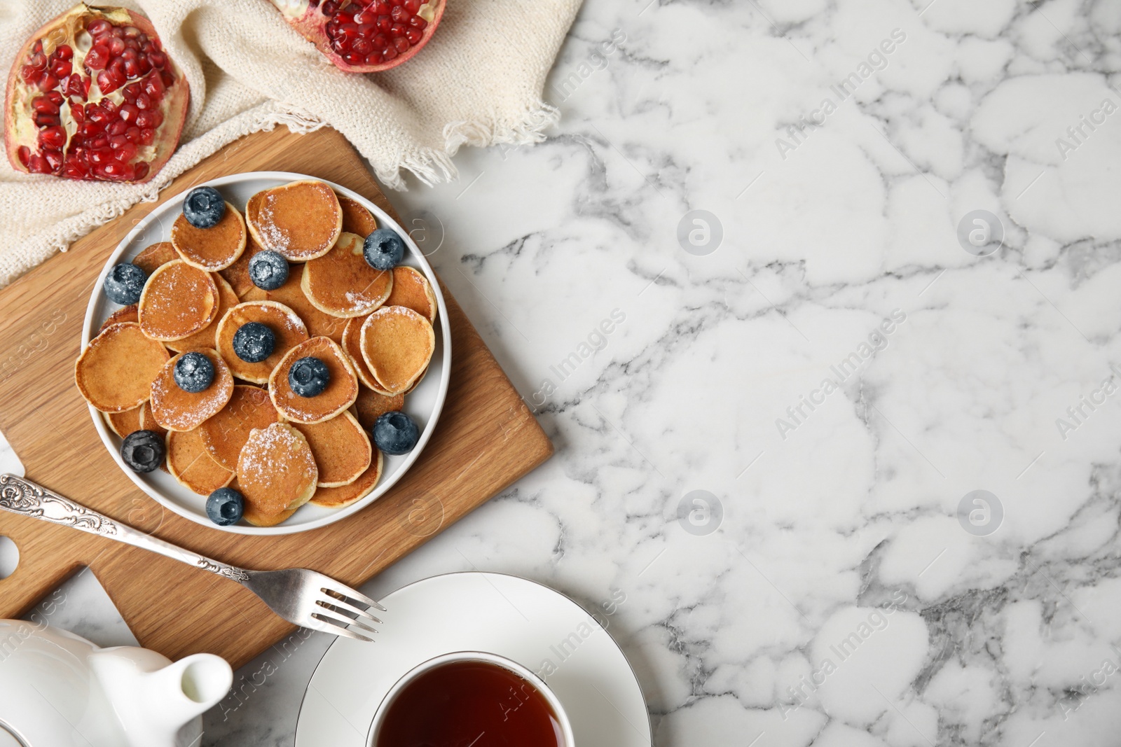 Photo of Delicious mini pancakes cereal with blueberries served on white marble table, flat lay. Space for text