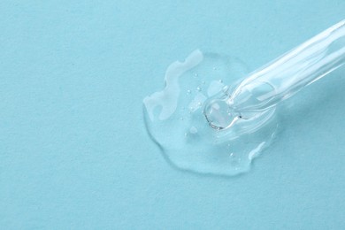 Photo of Dripping cosmetic serum from pipette onto light blue background, top view. Space for text