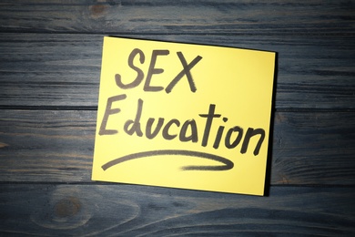 Note with phrase "SEX EDUCATION" on dark wooden background, top view