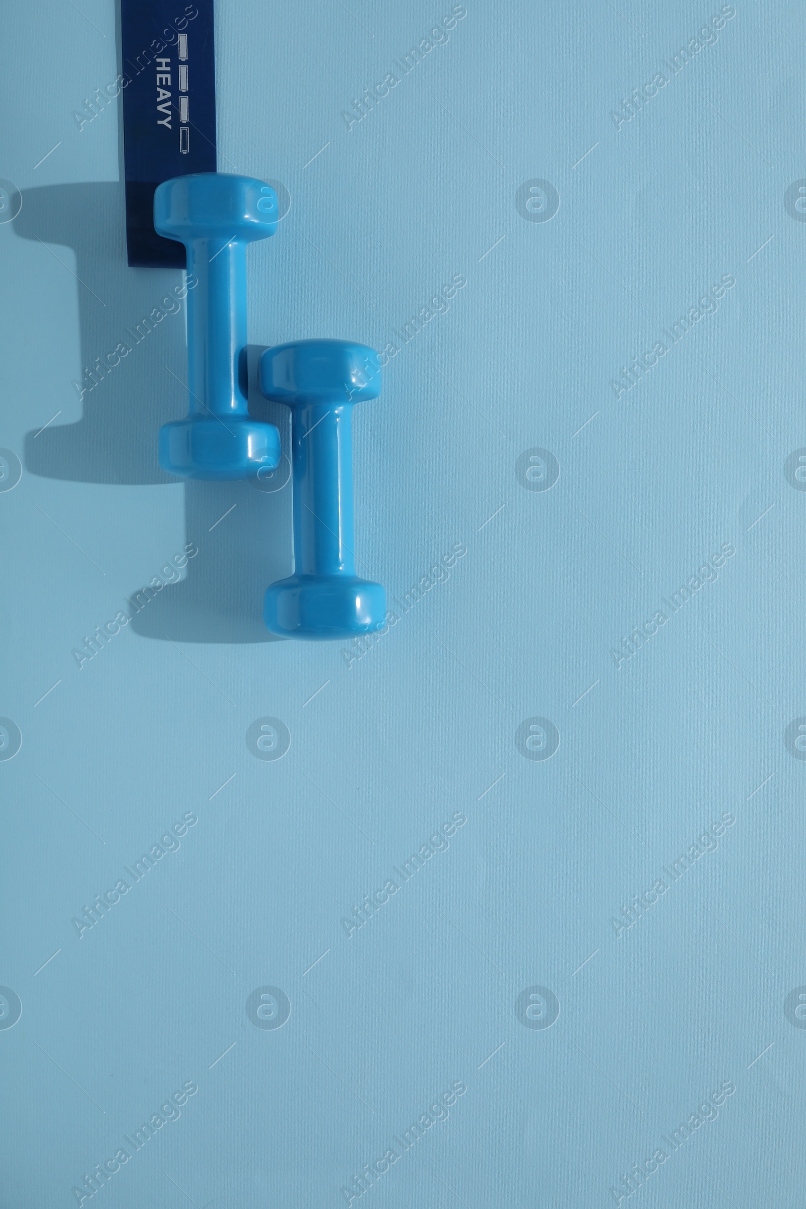 Photo of Two dumbbells and fitness elastic band on light blue background, flat lay. Space for text