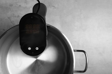 Photo of Sous vide cooker in pot on light grey table, closeup. Thermal immersion circulator