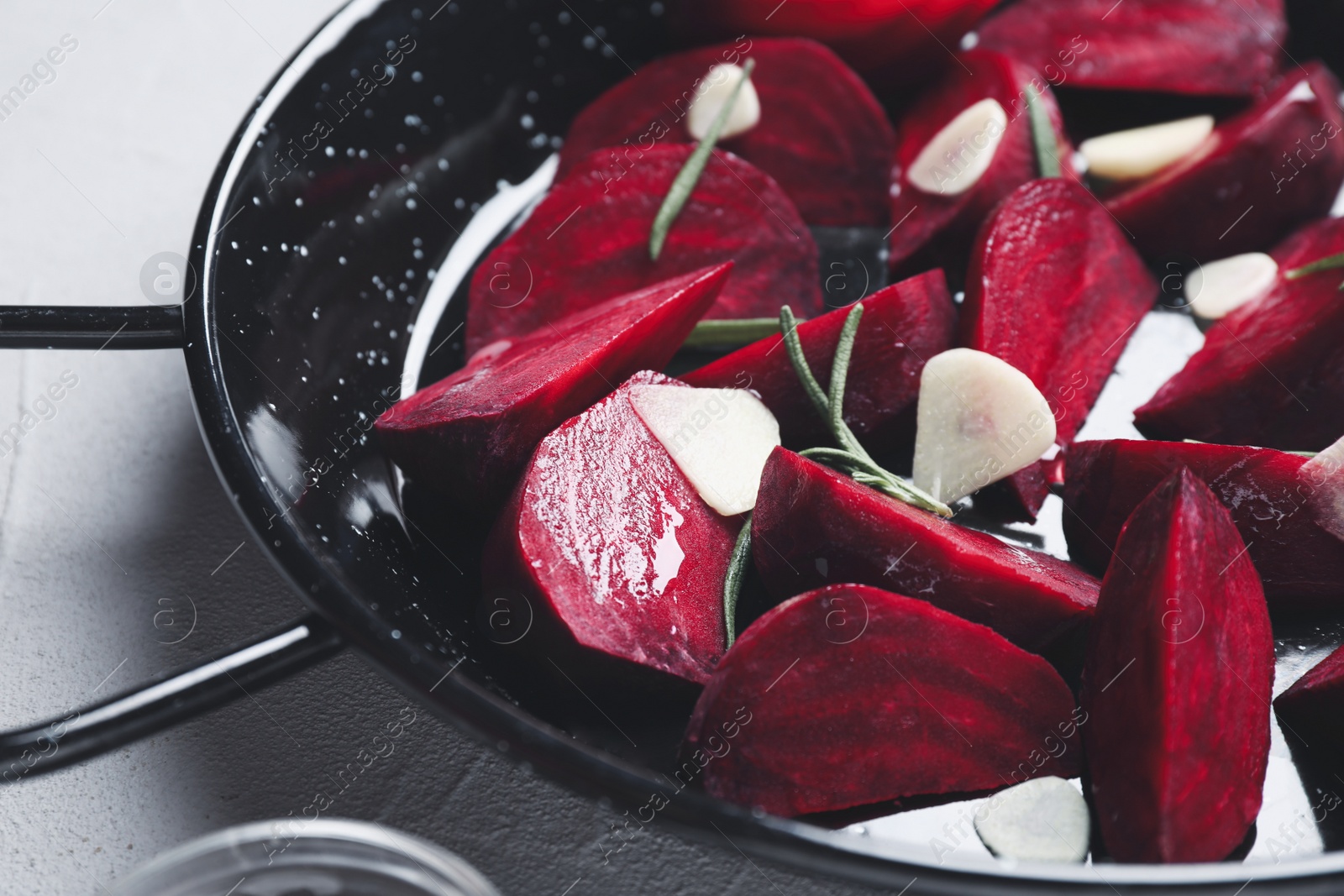 Photo of Slices of raw beetroot with garlic and rosemary in wok pan on white table, closeup