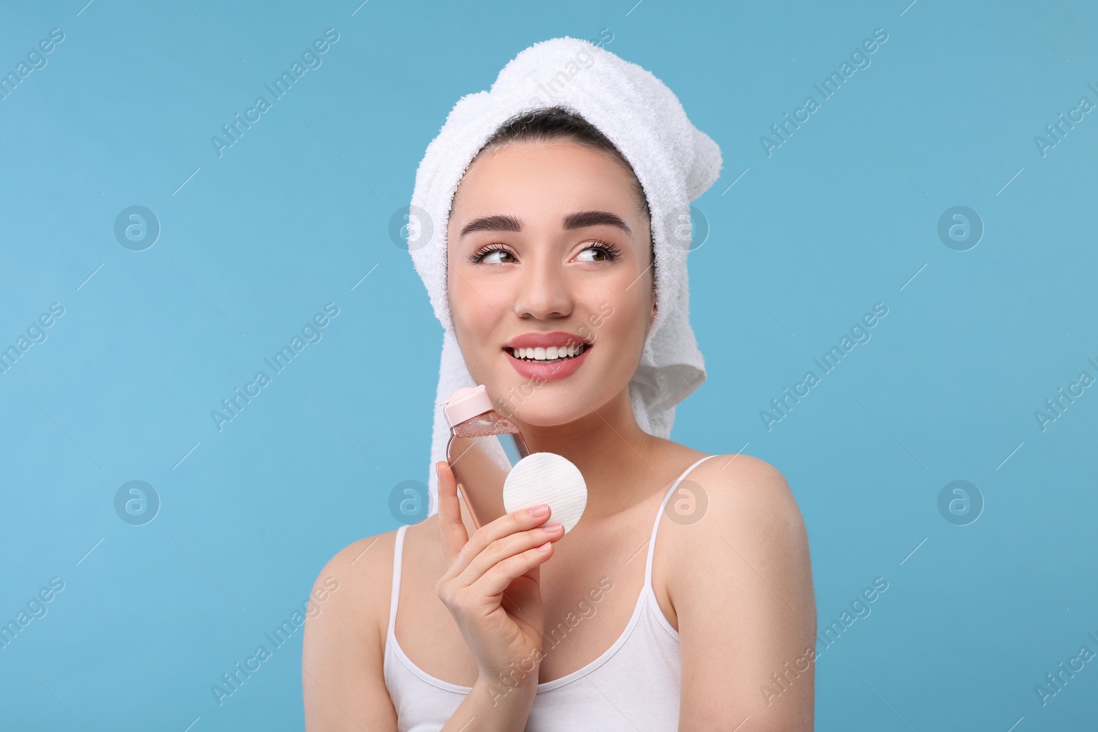 Photo of Beautiful woman with makeup remover and cotton pad on light blue background