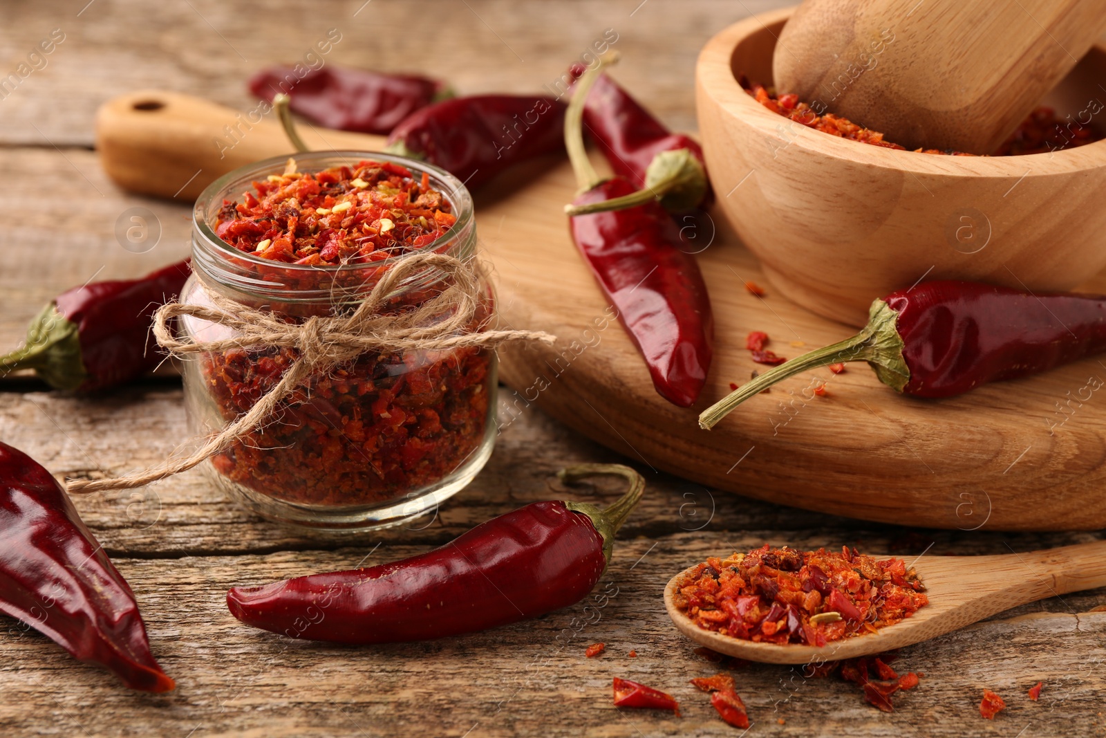 Photo of Chili pepper flakes and pods on wooden table, closeup