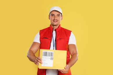 Photo of Happy young courier with envelopes on yellow background