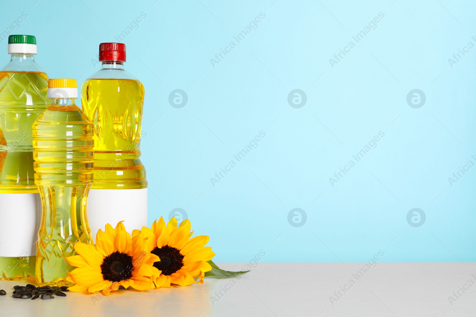 Photo of Bottles of cooking oil, sunflowers and seeds on white table, space for text