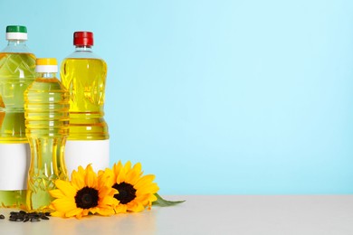 Photo of Bottles of cooking oil, sunflowers and seeds on white table, space for text