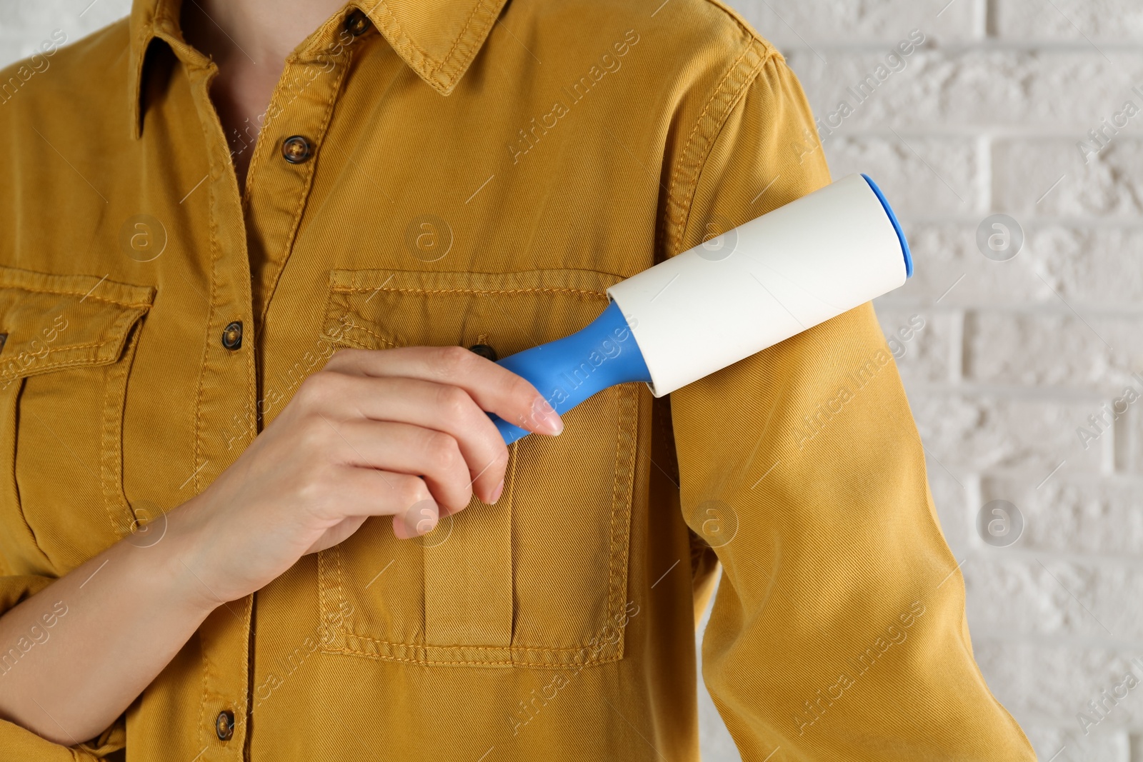 Photo of Woman cleaning yellow shirt with lint roller against white brick wall, closeup