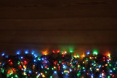 Photo of Colorful Christmas lights on wooden table, top view. Space for text