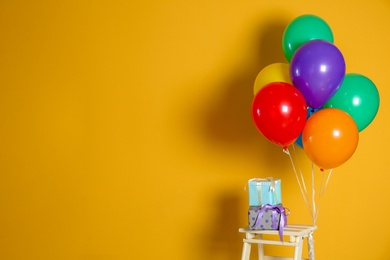 Photo of Bunch of bright balloons and gifts on stool against color wall. Space for text