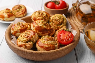 Fresh delicious puff pastry with tasty filling and tomato in bowl on white wooden table, closeup