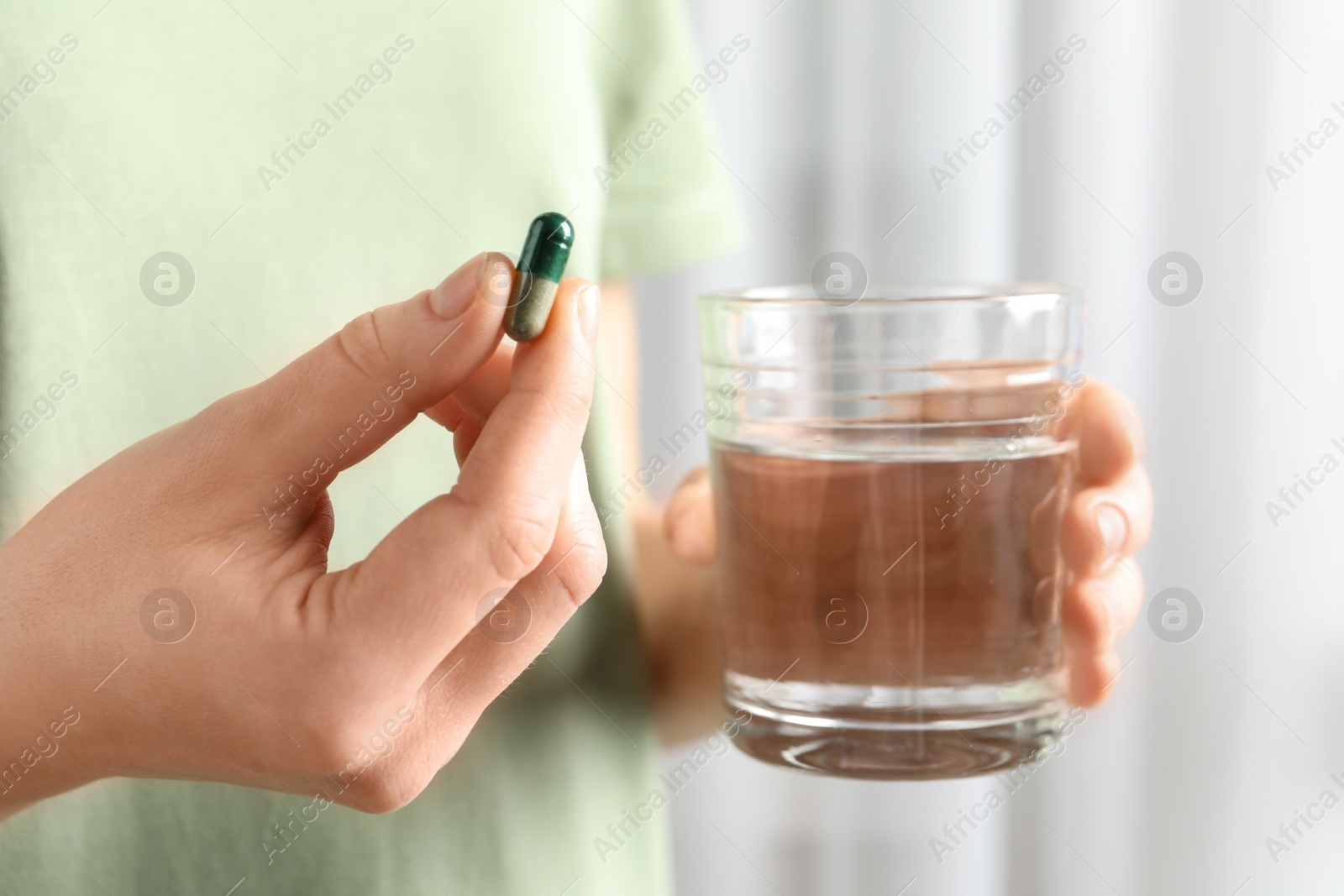 Photo of Woman holding spirulina pill and glass of water, closeup