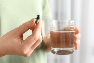 Photo of Woman holding spirulina pill and glass of water, closeup