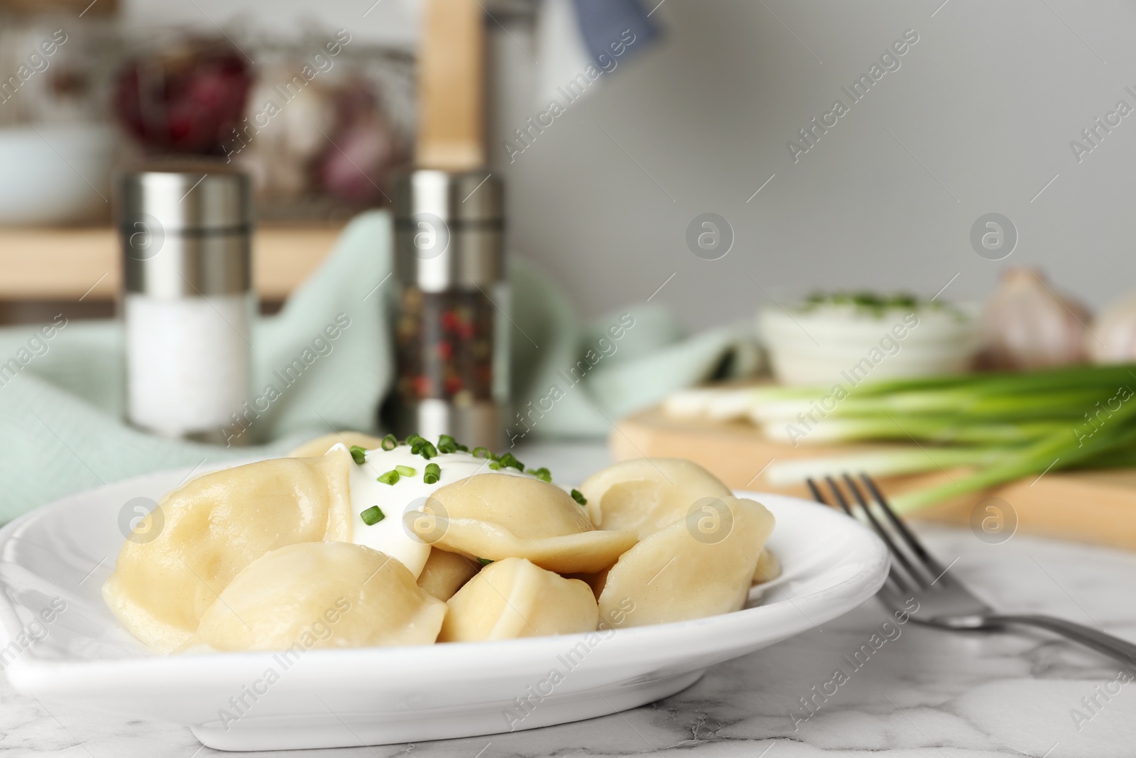 Photo of Delicious cooked dumplings with sour cream on white marble table, closeup