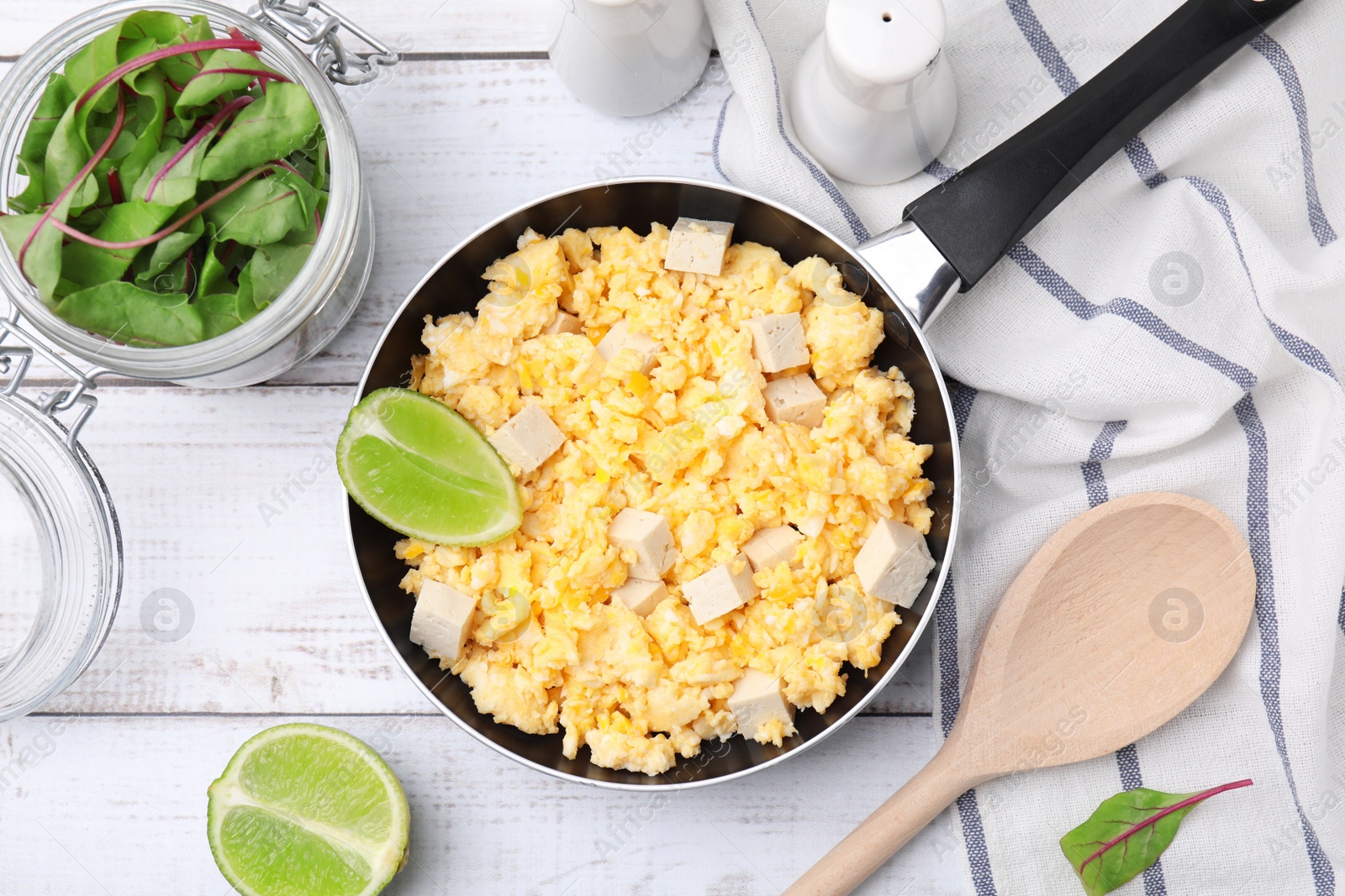 Photo of Frying pan with delicious scrambled eggs, tofu and lime on white wooden table, flat lay