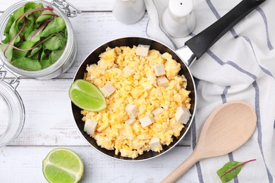 Frying pan with delicious scrambled eggs, tofu and lime on white wooden table, flat lay