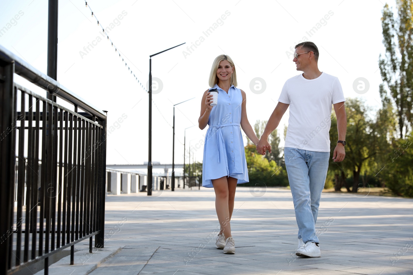 Photo of Happy couple with drink walking along city street on summer day