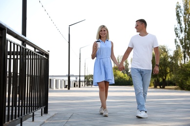 Happy couple with drink walking along city street on summer day