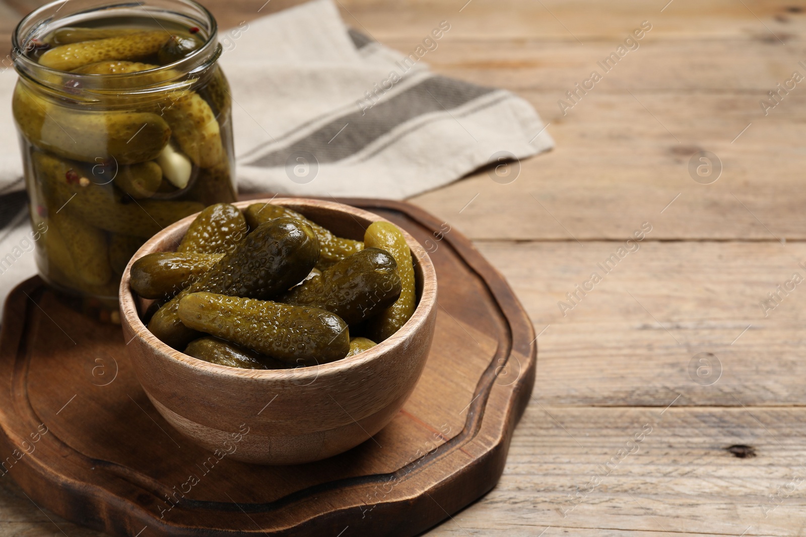 Photo of Tasty pickled cucumbers in jar and bowl on wooden table. Space for text