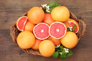 Photo of Wicker basket with fresh grapefruits and green leaves on wooden table, top view
