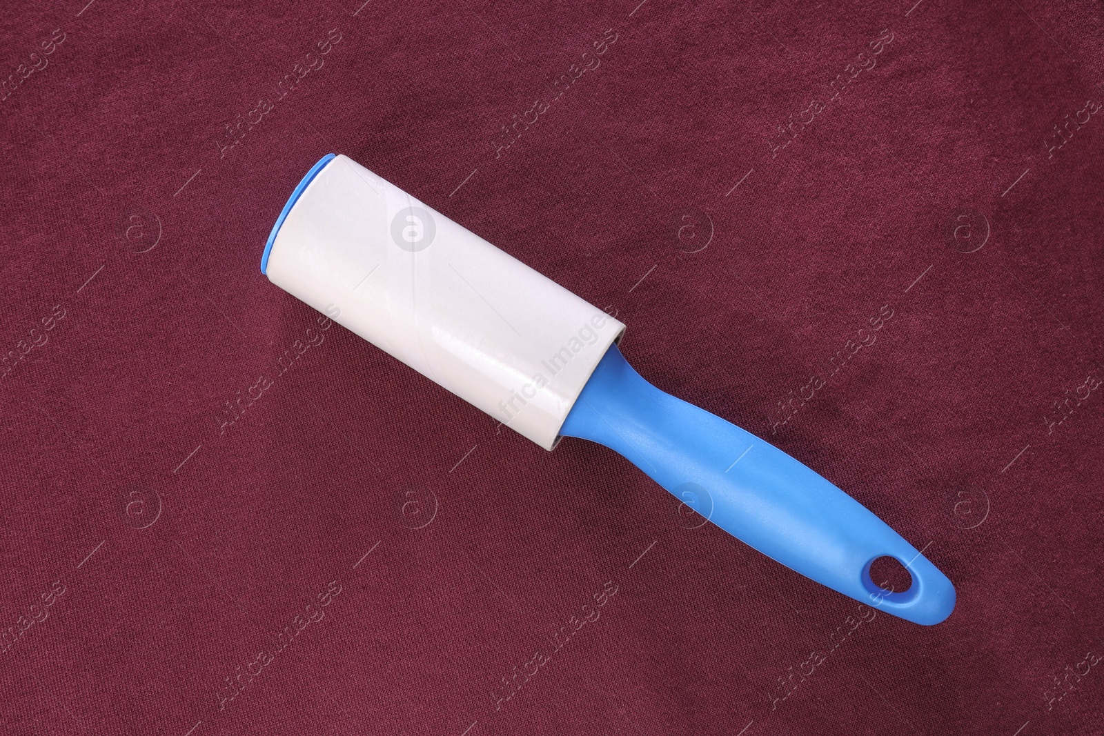 Photo of New lint roller with blue handle on red fabric, top view